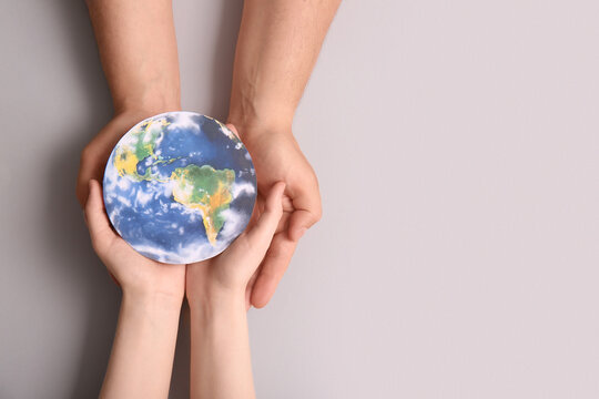 Female hands with paper planet Earth on grey background. World Oceans Day