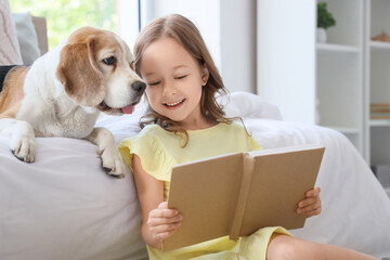 Obraz premium Cute little girl with Beagle dog reading book near bed in bedroom