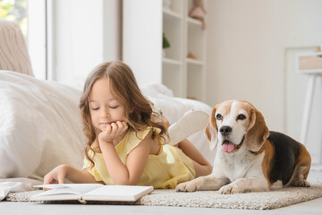 Obraz premium Cute little girl with Beagle dog reading book on floor in bedroom