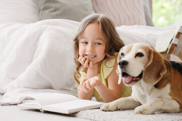 Obraz premium Cute little girl with Beagle dog reading book on floor in bedroom
