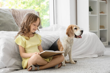 Obraz premium Cute little girl with Beagle dog reading book on floor in bedroom
