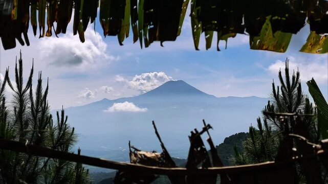 Artistic view of Mount Slamet volcano framed by tropical foliage and bamboo. Evocative storytelling shot for high-end travel and cultural content.
