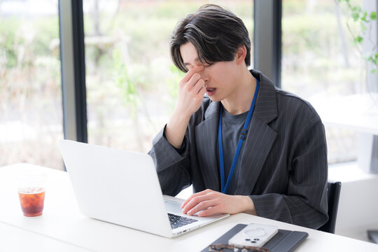 仕事の疲れで目を押さえる若手社員のストレスと体調不良のシーン　眼精疲労や目の疲れのビジネスイメージ