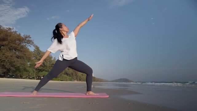 Asian woman practicing yoga reverse warrior pose on beach in Thailand. Healthy lifestyle outdoor scene ideal for fitness, wellness, travel and mindfulness content.