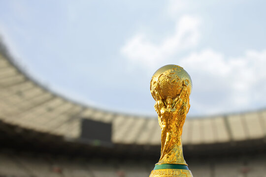 The golden World Cup trophy stands out in focus against the blurred background of a huge football stadium. A symbol of ultimate victory and sporting glory.