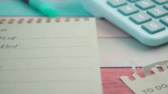 To do list written in notepad on wooden table with calculator and pen in cinematic motion.