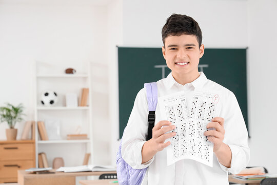 Upset teenage boy tearing answer sheet for school test with bad grade in classroom