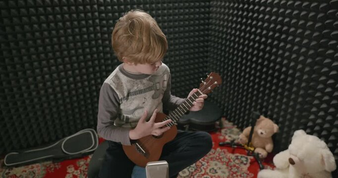 Boy Play Music on Ukulele Instrument in Home Studio. 4K 10-bit