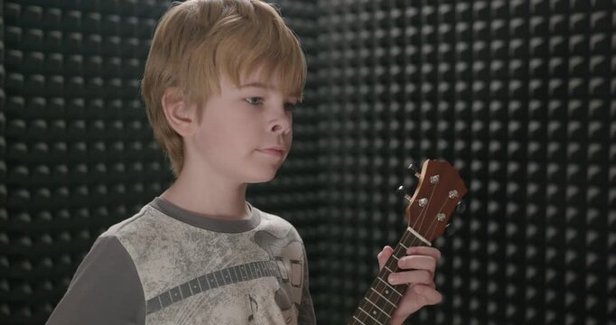 Boy Play Music on Ukulele Instrument in Home Studio. 4K 10-bit