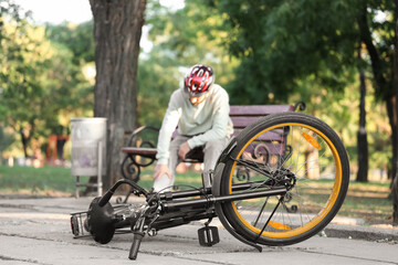 Fototapeta premium Young man sitting on bench after falling off his bike in park