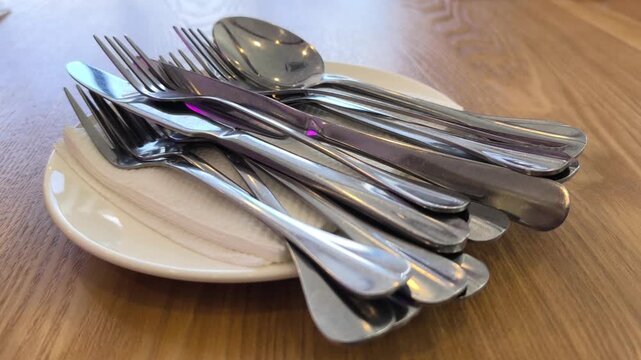 Clean silverware rests neatly on a white plate and napkin. The cutlery is set on a dining table. Everything is ready for the upcoming meal service.