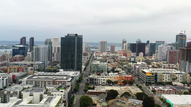 Drone pulling back from the downtown San Diego skyline revealing surrounding buildings and city layout in morning light.