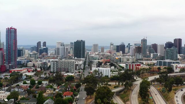 Drone flying toward downtown San Diego with a trolley moving through the background during early morning.