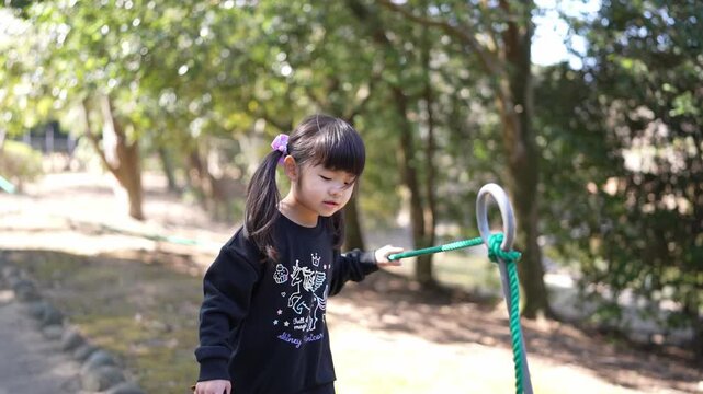 Little girl explores outdoors with a green rope. She concentrates as she pulls the rope through a wooded path. Dense trees frame the scene with soft natural light