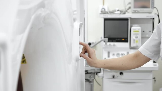 Medical worker pressing control button on tomography scanner to start diagnostic imaging procedure in modern hospital environment.