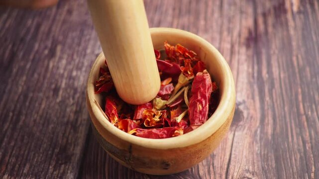 Grinding dried peppers in a wooden bowl