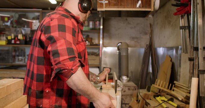 Joiner process. Furniture making. Man with ear protectors smoothing wood on thickness planer. Saw dust flying in industry interior.