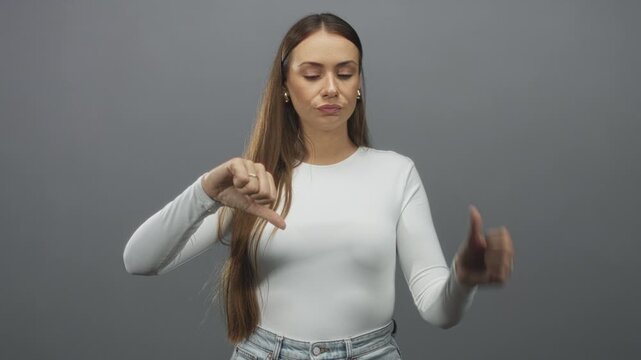 Woman showing thumb down gesture with neutral expression and long hair in studio; disapproval rejection.