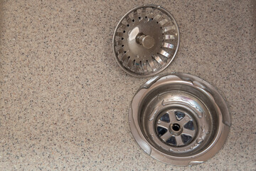 Obraz premium Stainless steel sink drain with strainer and drain cover on a textured countertop surface in a modern kitchen setting