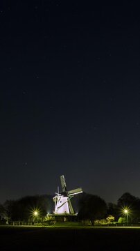Beautiful vertical time lapse of a traditional windmill in the Netherlands at night with the constellation moving over the windmill and shooting stars.