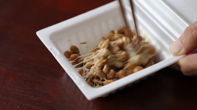 Mixing some "Natto" (fermented soybeans) with wooden chopsticks in a styrofoam container.