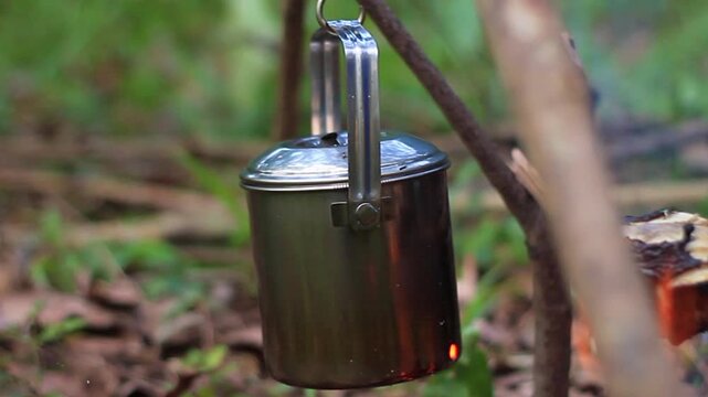Boiling water in a stainless steel mug over a small wood campfire while camping in the forest.