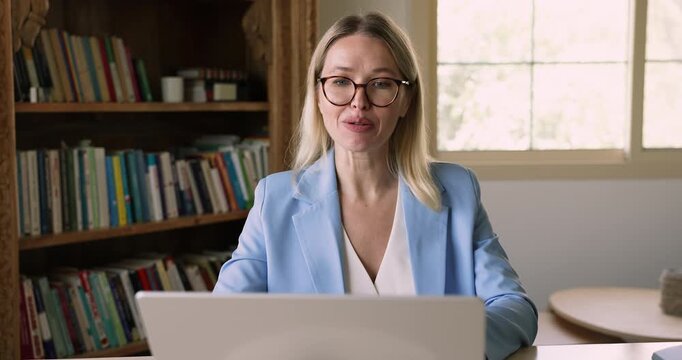 Confident Caucasian online teacher woman in glasses giving training webinar on Internet, speaking at laptop computer, talking on video conference call, using technology for remote communication