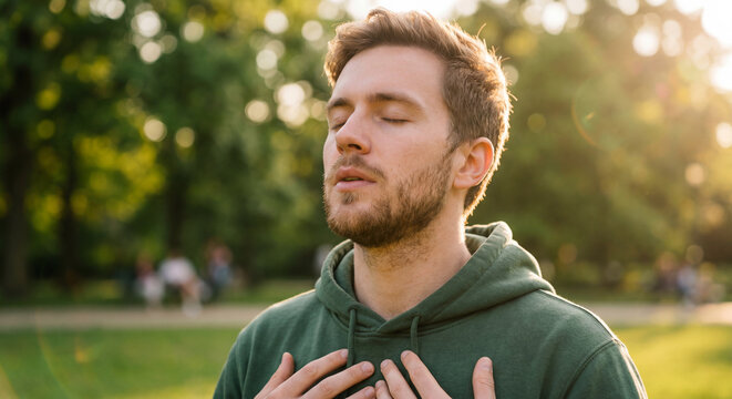 Young man practicing deep breathing meditation outdoors in sunlight for mental health and relaxation