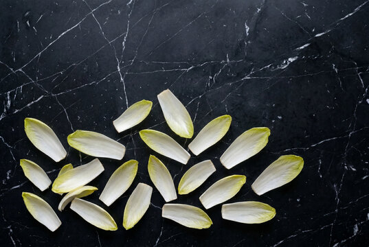 Fresh raw belgian endive leaves arranged on a black marble surface