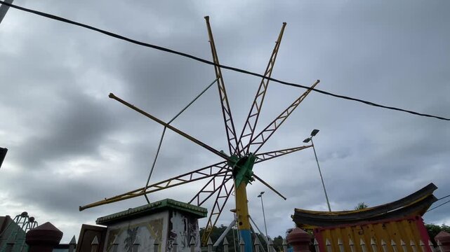 A stationary paratrooper umbrella ride under installation at a funfair with the metal structure against a cloudy evening sky.