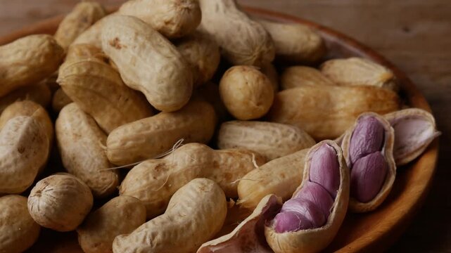 Boiled peanuts in shell with purple violet skin kernels revealed on wooden plate on rustic wood table, healthy traditional Asian snack nutrition closeup