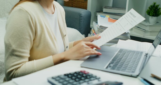 Individual Reviewing Financial Reports.An Asian individual reviews financial reports and property rates, calculating income and expenses with serious dedication using technology.