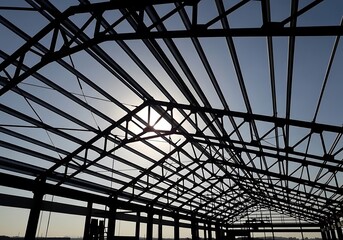 Fototapeta premium Steel framework of an unfinished building with exposed metal beams and trusses against a clear sky