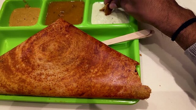 India hand eating mysore dosa with sambar and coconut chutney in restaurant tray