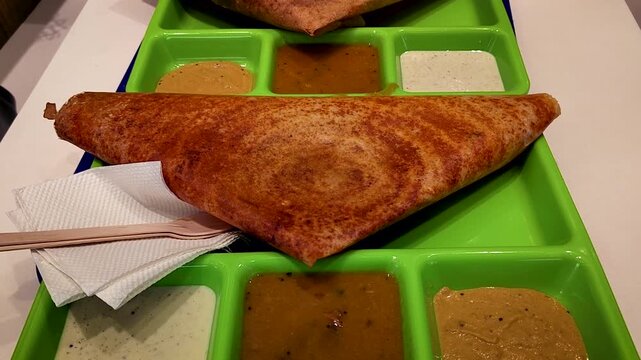 India mysore dosa served with sambar and coconut chutney on tray in restaurant.