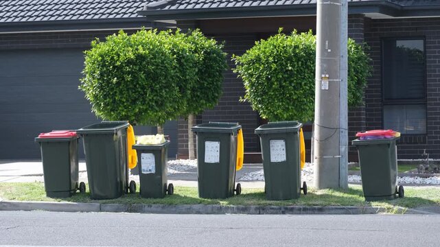 Row of household waste bins lined up on a suburban street curb in Melbourne, Australia, in front of a modern residential home. council waste collection, recycling systems, and living routines.