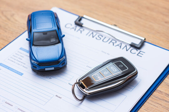 Close up of automobile insurance application form with miniature car model and electronic keychain. Concept vehicle protection, motor legal services, loan agreement and financial security.