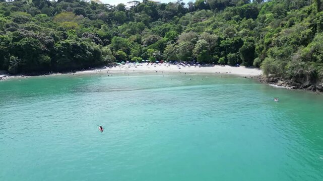 Aerial shot of a paradisiacal white sand beach in turquoise waters full of tourists on the Pacific coast of Costa Rica at sunset
