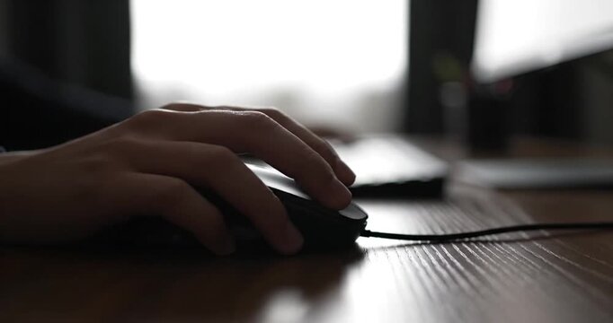 Close-up of a hand using a computer mouse, with a blurred background of a workspace