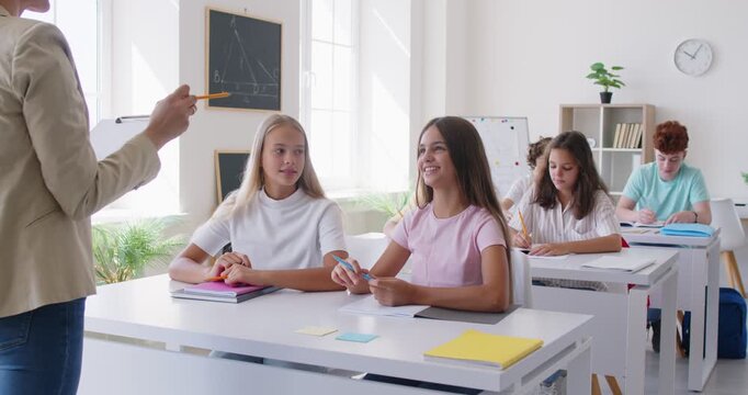 Students raise their hands, signaling their desire to answer teacher questions during lesson. Schoolchildren sit at desks in school classroom, ready to take notes or answer questions. 4k footage.