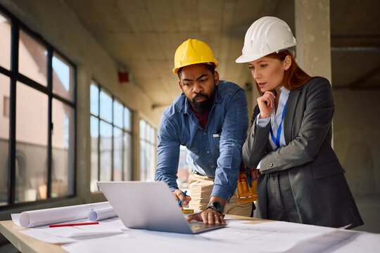 Black worker and female project manager working on laptop at construction site.