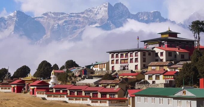 Aerial drone shot of the Everest Himalayan range wrapped in clouds with Tengboche Monastery, rural buildings, stupa and scattered green trees along the Everest Base Camp trekking route in Nepal.