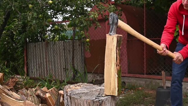 man chopping log with axe in backyard. Axe strikes log, but it does not split. person in red hoodie focuses on chopping, natural outdoor lifestyle, closeup. routine of rural life. natural biofuels