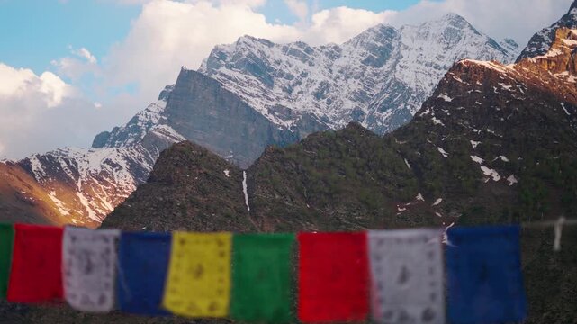 4K shot of snowy Himalayan mountain peak with clouds above it and defocused Buddhist prayer flags in front as seen from Khangsar village in Lahaul and Spiti district, Himachal Pradesh, India.