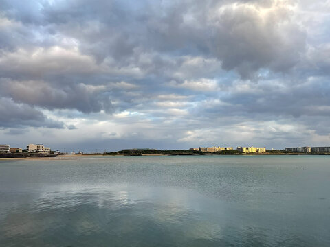 A wide-angle view of a serene coastal bay with modern buildings and resort houses under a dramatic cloudy sky in Jej