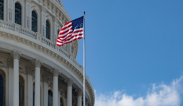 American flag near capitol with classical columns. Capitol with american flag near government building. Us flag on capitol as freedom symbol. Capitol with american flag under sky.