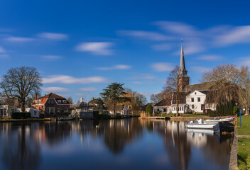 Fototapeta premium Waterside village with church steeple, boats and reflections on calm water