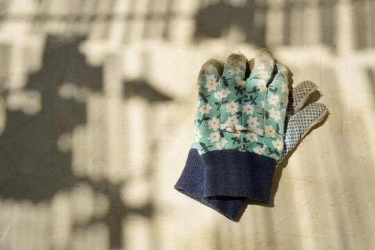 Vieux gants de jardin &agrave; motifs floraux en coton, pos&eacute;s sur une table, sous l'ombre des canisses