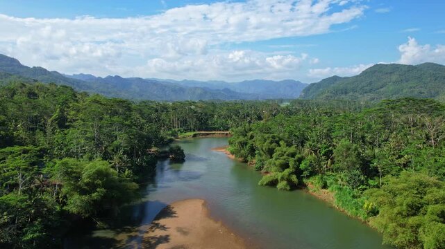 Aerial drone footage of Taman river in Ngadirojo, Pacitan regency, Java island, Indonesia, with beautiful turquoise color, forest around, in a valley with hills in the background, the town behind