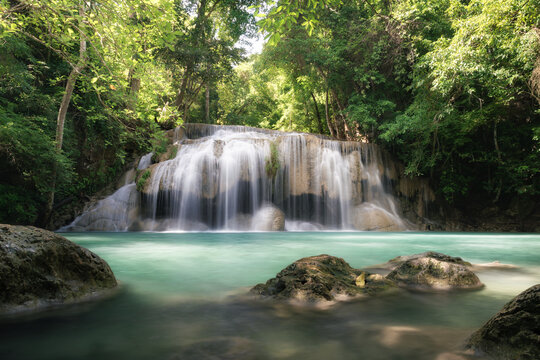 Erawan Waterfall Tier 2 at Wang Macha is popular travel destination in Kanchanaburi Province, Thailand, waterfall flows over limestone tiers into clear turquoise pool, surrounded by lush green forest.